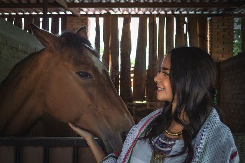 Free A woman smiles warmly while patting a horse inside a stable. Stock Photo