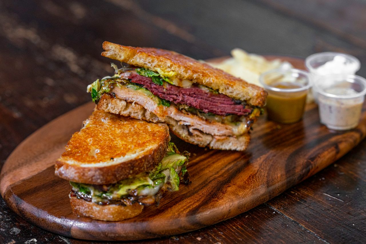 Layered deli sandwich with cured meat and cheese on a wooden board, showing the interior stack