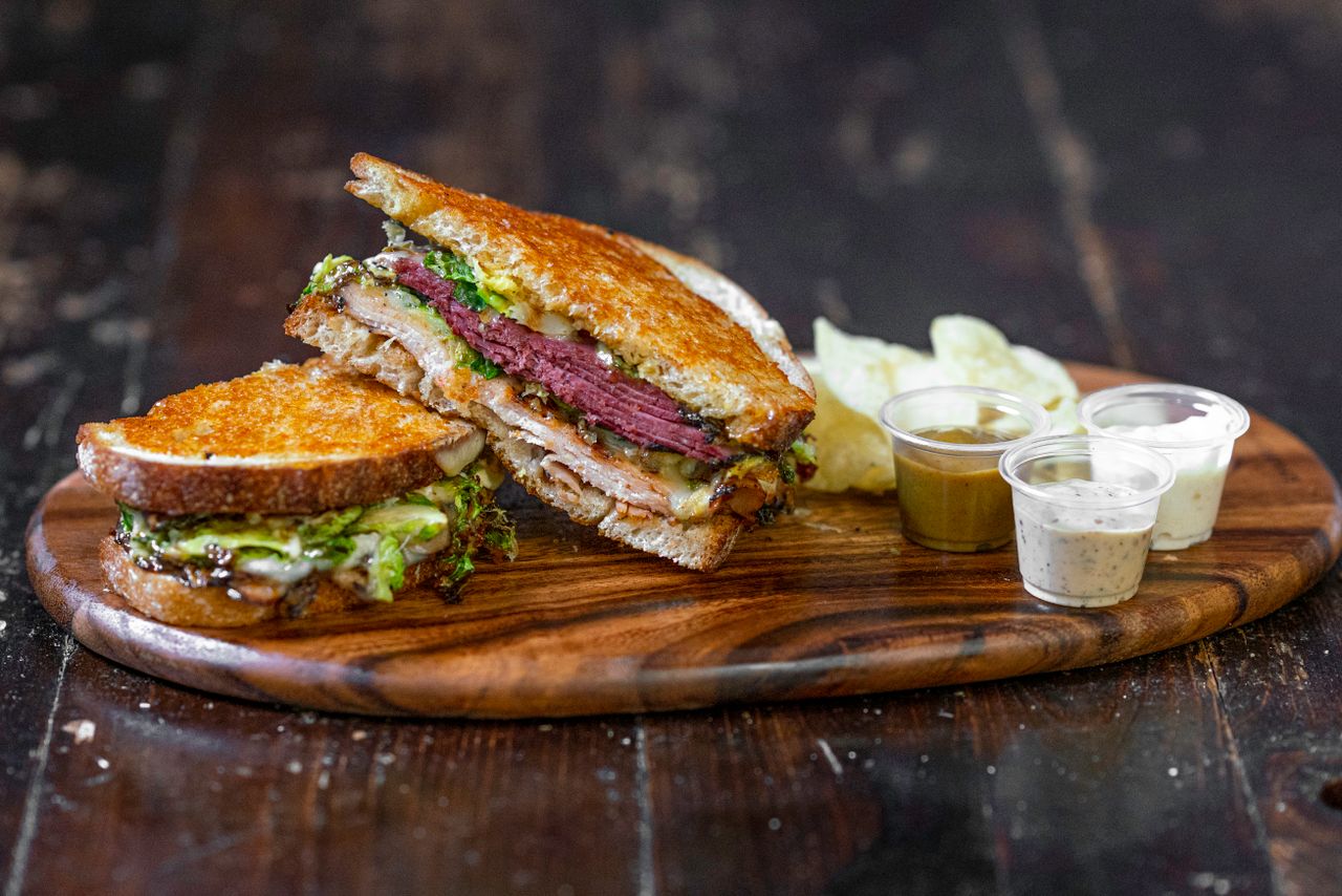 Grilled deli sandwich sliced and plated with dipping sauces, wooden serving board