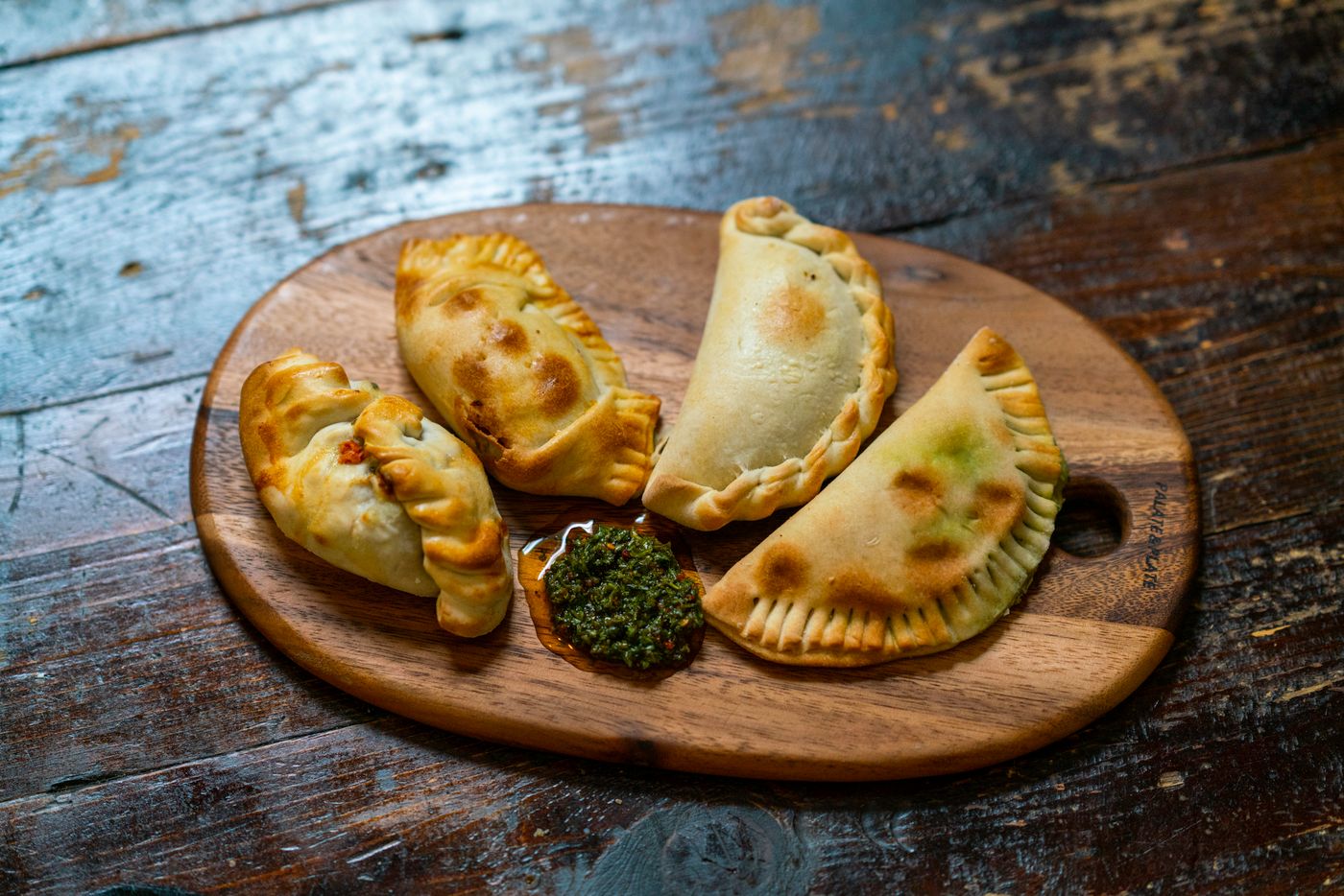 Baked empanadas with chimichurri sauce on a wooden board, a classic Fiestas Patrias pairing for Chilean red wine