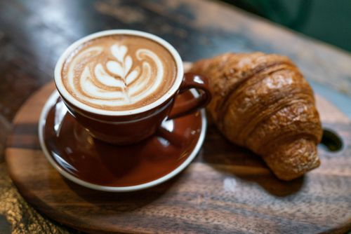 Free A delicious cappuccino with latte art served with a fresh croissant on a wooden tray. Stock Photo