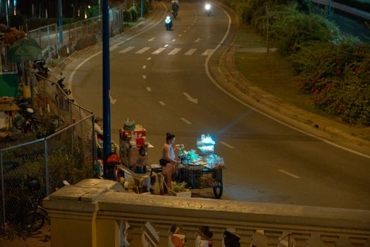 A woman street vendor operates a small cart on an empty city street at night.