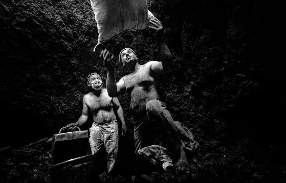 Two shirtless coal miners work together underground, emphasizing teamwork and labor.