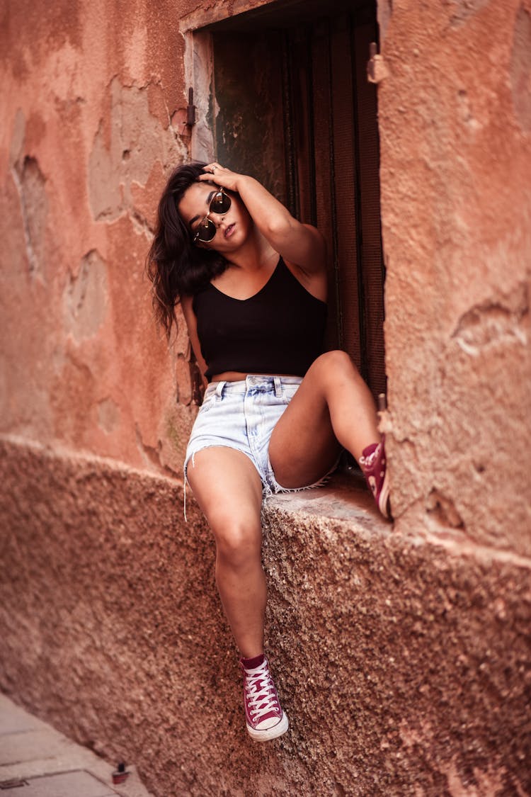 Young Woman In A Summer Outfit Sitting On The Side Of A Building 