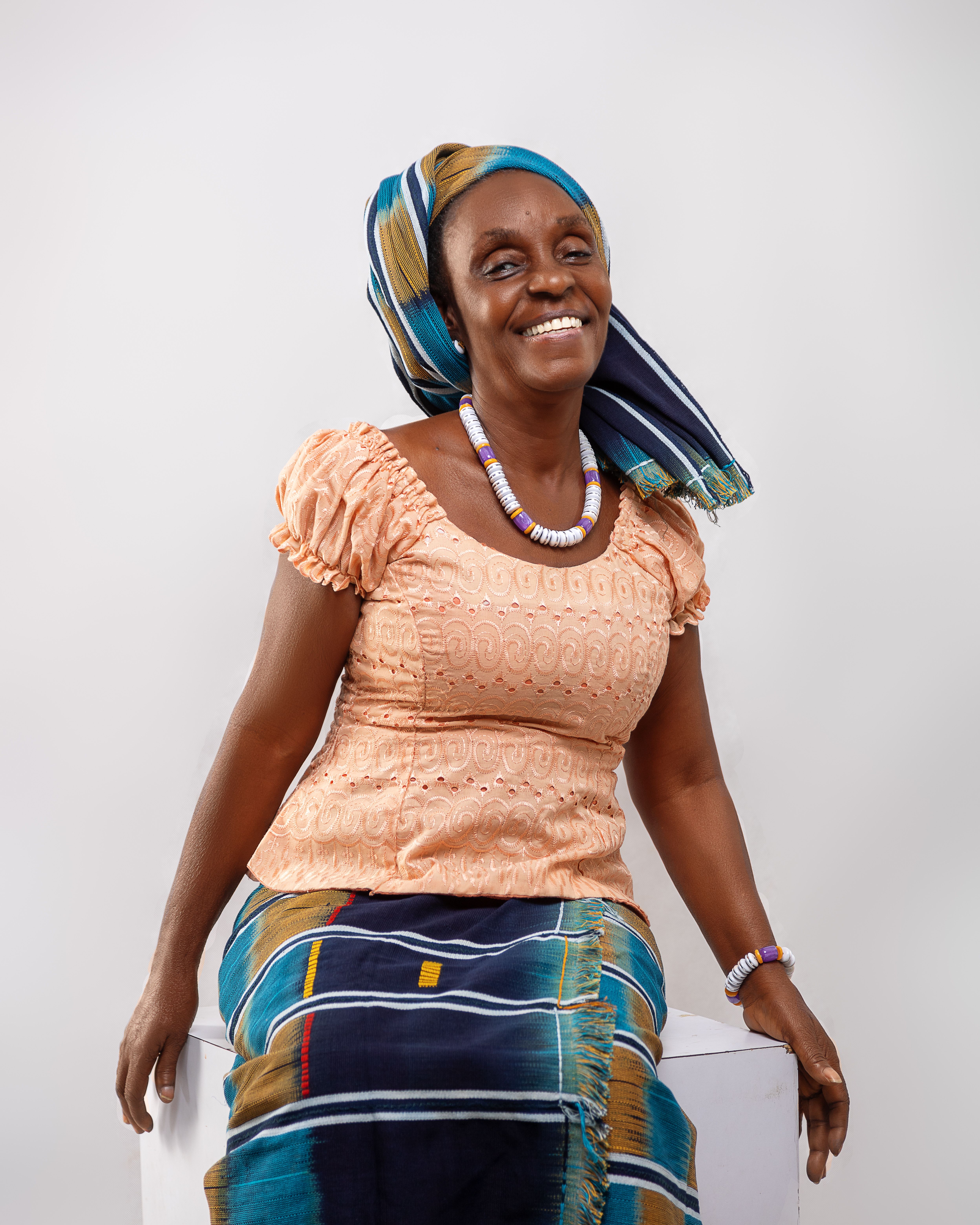African woman in vibrant tribal wear with headwrap and necklaces, smiling.