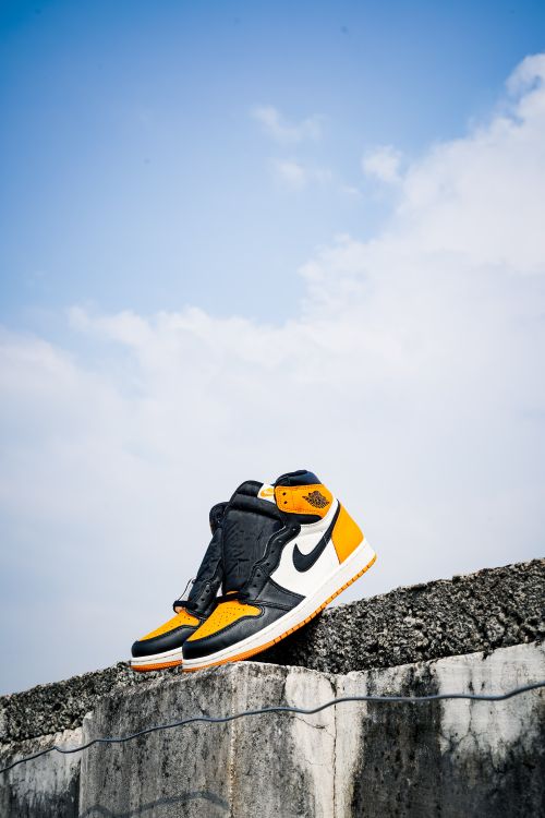 Free Pair of trendy sneakers on a wall under a bright blue sky, perfect for fashion and lifestyle themes. Stock Photo