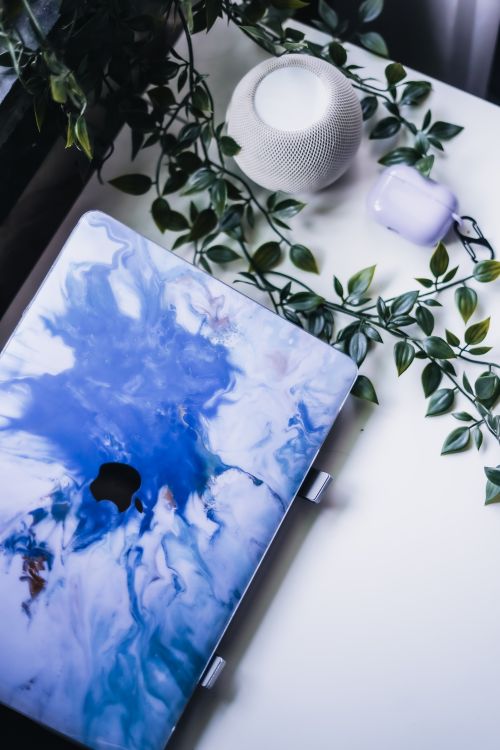Free Modern workspace setup featuring a laptop with a blue abstract design beside a smart speaker and plants. Stock Photo