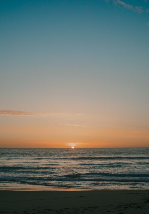 Free Tranquil beach sunset with soft ocean waves and clear sky, perfect for a peaceful atmosphere. Stock Photo