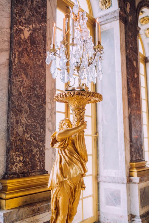 Free A stunning golden sculpture holding a chandelier inside the luxurious palace of Versailles. Stock Photo