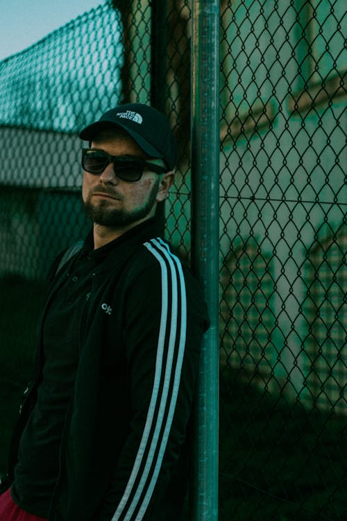 Man Wearing Sunglasses Leaning on Chain Link Fence