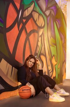 Woman sitting with basketball against colorful graffiti wall in Bauru, Brazil, smiling.
