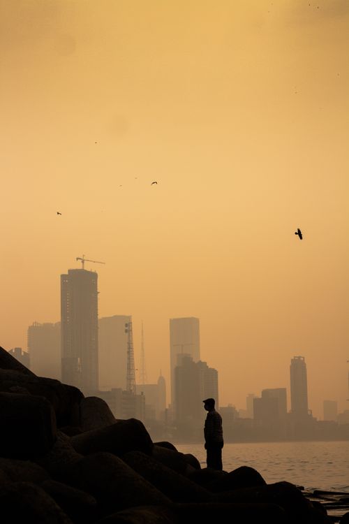Free A man stands silhouetted against the Mumbai skyline at sunset, creating a dramatic coastal scene. Stock Photo