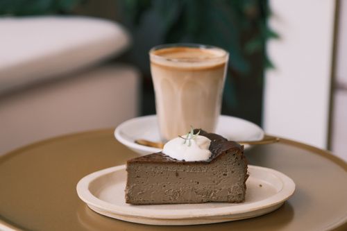 Free A slice of chocolate cake topped with cream served with a cappuccino in a cozy indoor cafe setting. Stock Photo