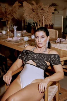 Fashionable woman in a stylish bodysuit sits elegantly at a chic restaurant setting.