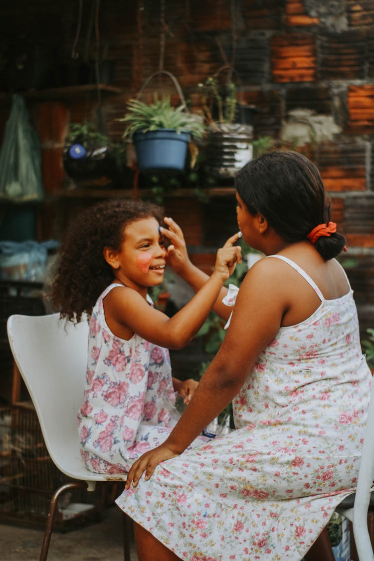 Woman And Girl Putting Face Paint On Each Other