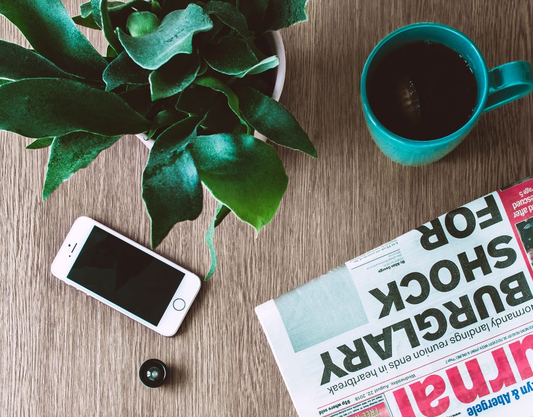 Flat lay of a coffee mug, folded newspaper and a plant on a table — photo by Lisa Fotios on Pexels