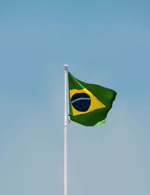 Free A Brazilian flag flutters on a flagpole against a clear blue sky in Brasília, Brazil. Stock Photo