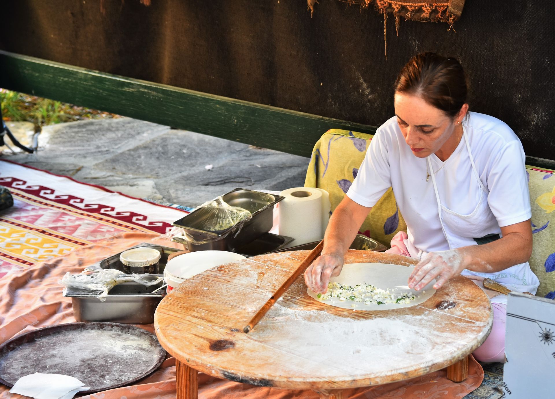 Woman preparing dough with filling on a wooden table, showcasing food preparation skills.
