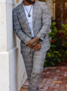 African American man in a plaid suit leans against a wall outdoors. Fashionable and casual.