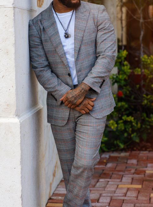 Free African American man in a plaid suit leans against a wall outdoors. Fashionable and casual. Stock Photo