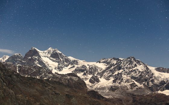 Majestic snow-capped mountains beneath a multitude of stars, capturing a serene winter night.