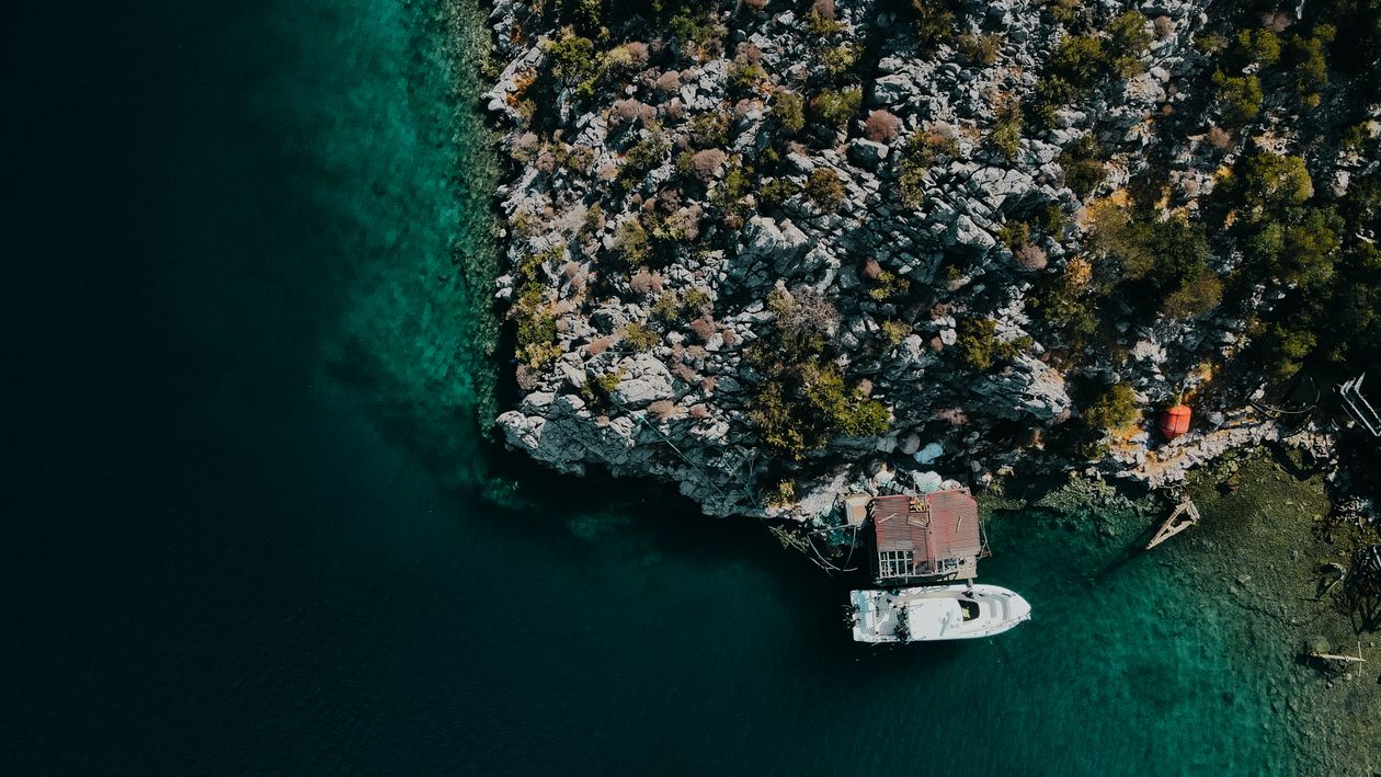 Aerial Footage of a Dark Turquoise Sea and Rocky Coast with a Boat ...