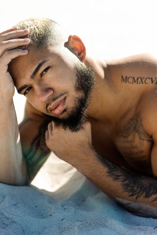 Free Close-up portrait of a bearded man with tattoos posing on sandy beach. Stock Photo