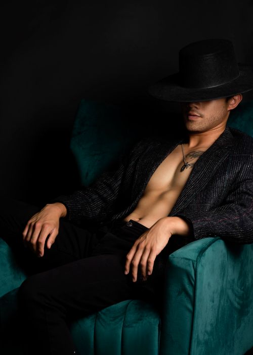 Free An adult male in a fashionable outfit and hat sits on a green sofa against a black background. Stock Photo