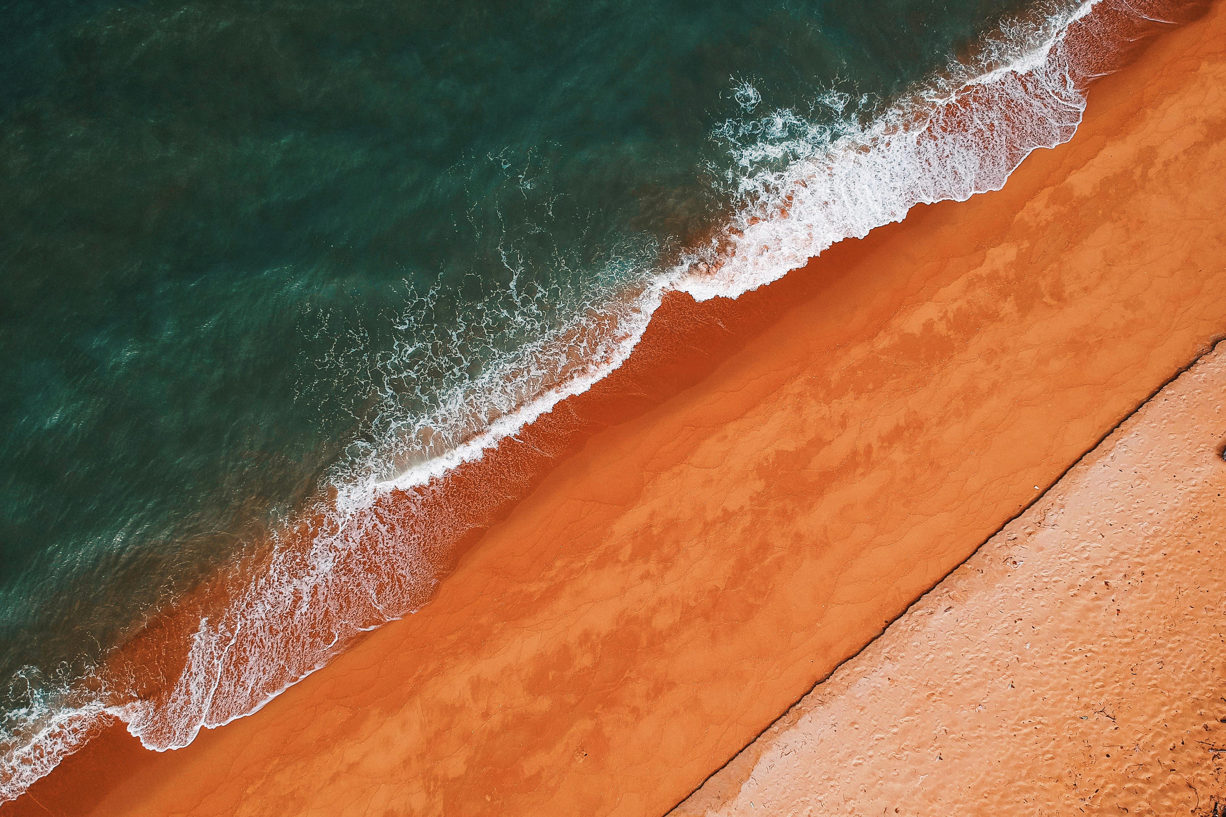 Explore the striking contrast of turquoise waves meeting vibrant orange sands from an aerial perspective.