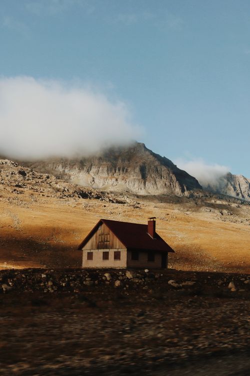 Wooden cabin in the foreground below a rocky mountain under a blue sky