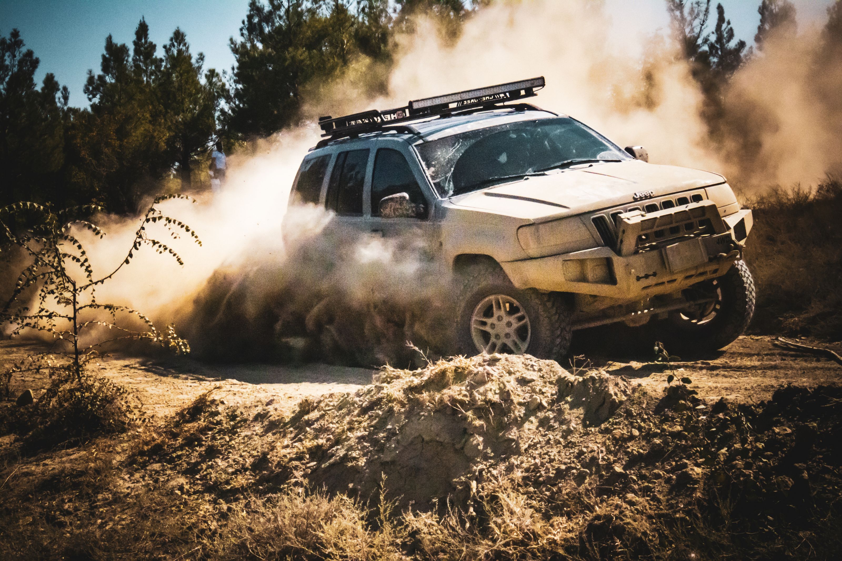 An SUV speeds through a dusty dirt road in a forest setting, showcasing off-road capabilities.