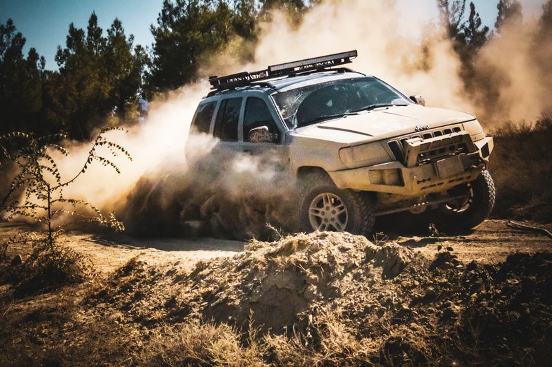 An SUV speeds through a dusty dirt road in a forest setting, showcasing off-road capabilities.