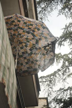 A low angle view of a patterned umbrella on a balcony next to tree branches on an overcast day.