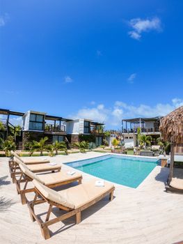 A stunning tropical resort featuring a crystal-clear swimming pool and relaxing sun loungers under a bright blue sky.
