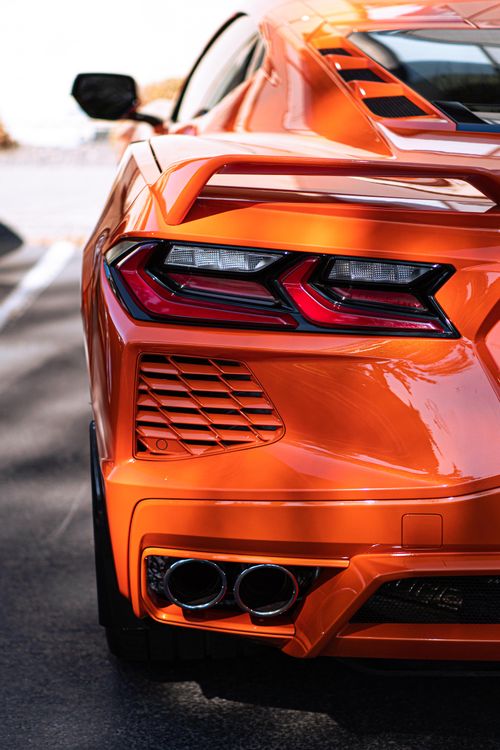 Free Captivating rear view of an orange sports car parked on a sunlit road, showcasing its sleek taillights and exhaust design. Stock Photo