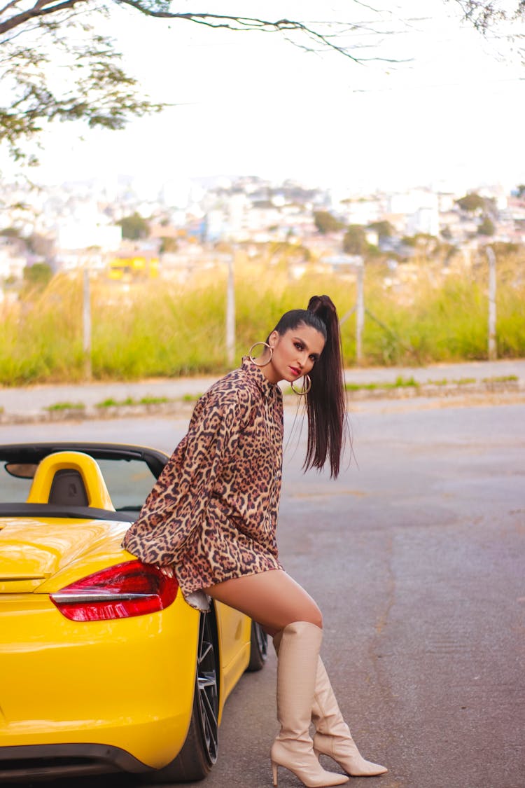 A Woman In A Leopard Print Outfit Leaning On A Yellow Convertible Car