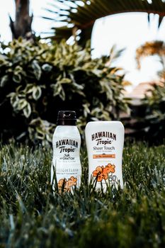 Close-up of Hawaiian Tropic sunscreen bottles on grass, ideal for summer outdoor use.