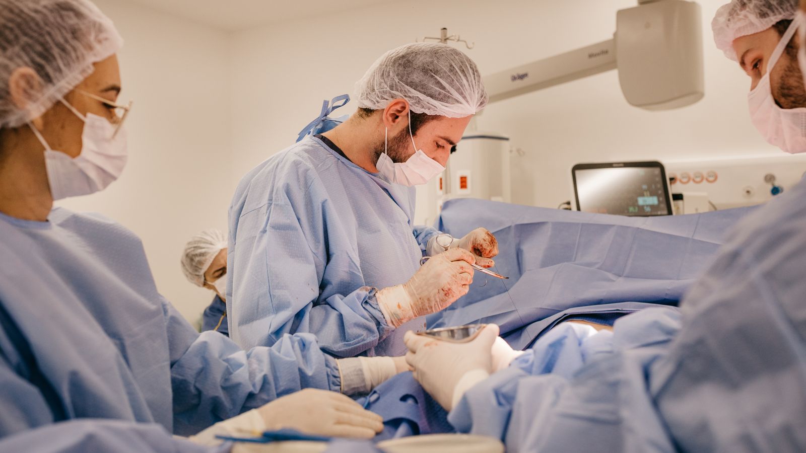 Surgeons and nurses collaborating during a surgical procedure wearing protective gear in a hospital operating room.