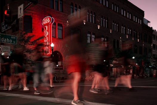 Blurred pedestrians crossing Idaho Street at night with vibrant neon lights in the background.
