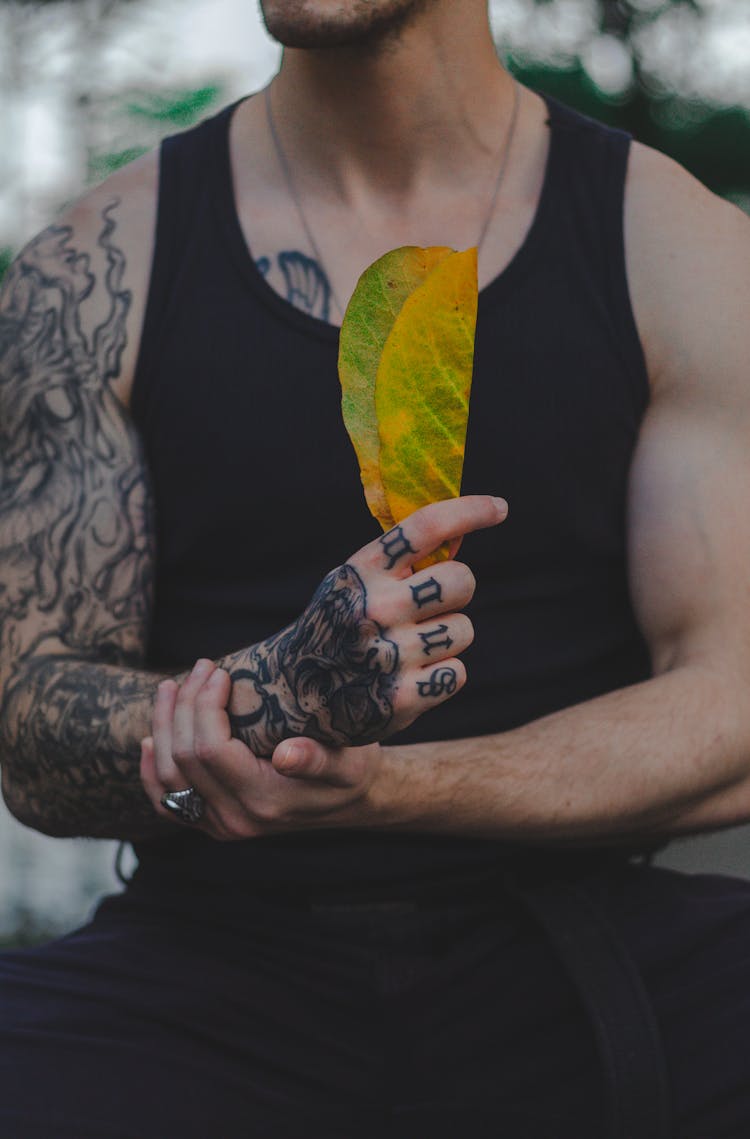 Man In Black Sleeveless Shirt Holding A Green And Yellow Leaf