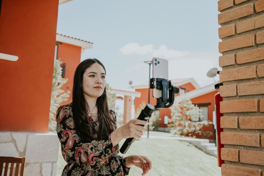 Young woman using a smartphone on a stabilizer for video recording outdoors.