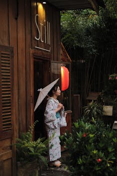 A woman in a kimono holds an umbrella beside a traditional building, depicting cultural beauty.