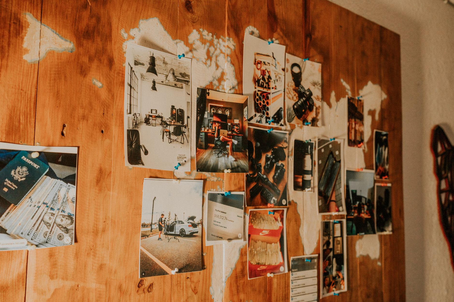 A collection of travel photos pinned on a wooden map-themed wall, evoking adventure and nostalgia.