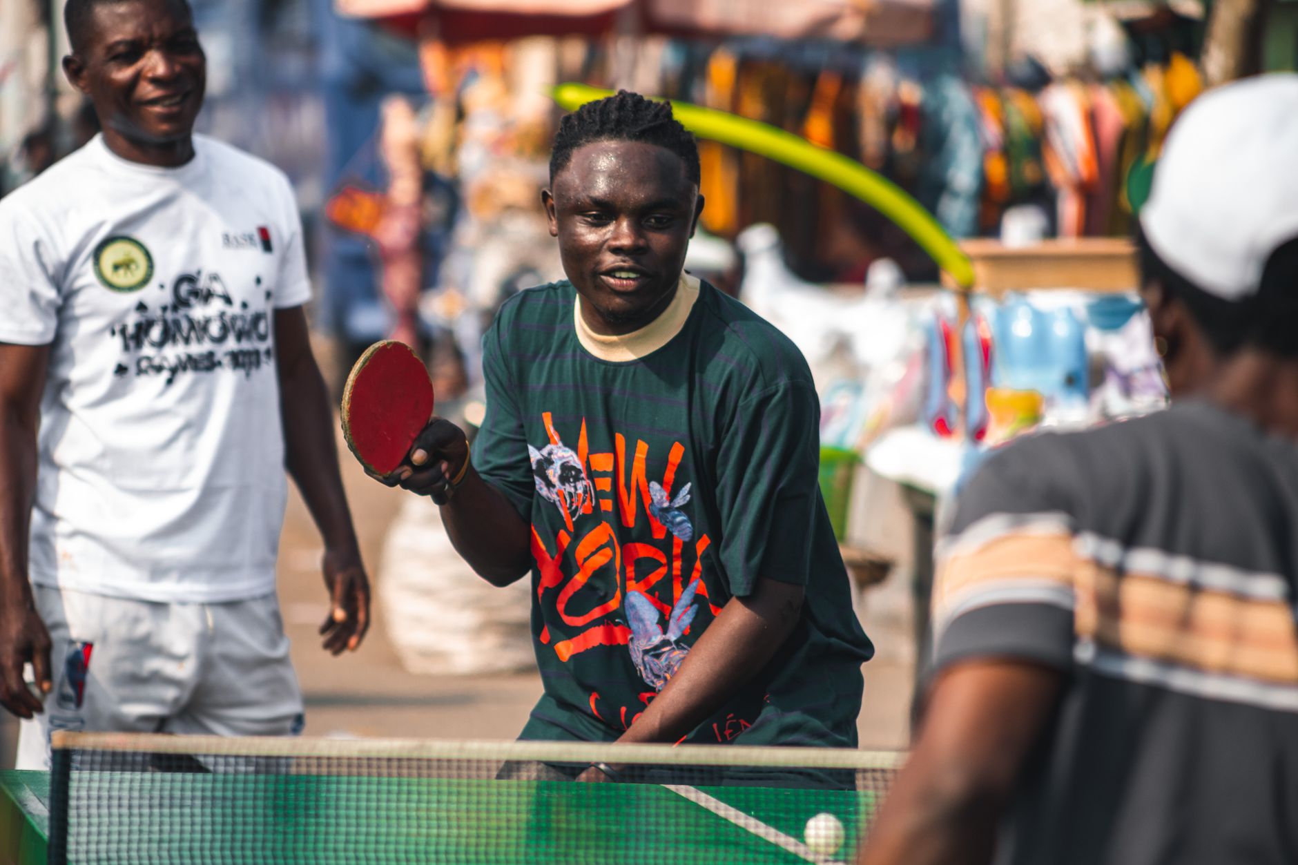 Young men playing table tennis on a vibrant street in Accra, Ghana, enjoying a sunny day.