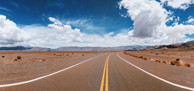 Empty desert road in Tinogasta, Catamarca, Argentina with vibrant sky and clouds.