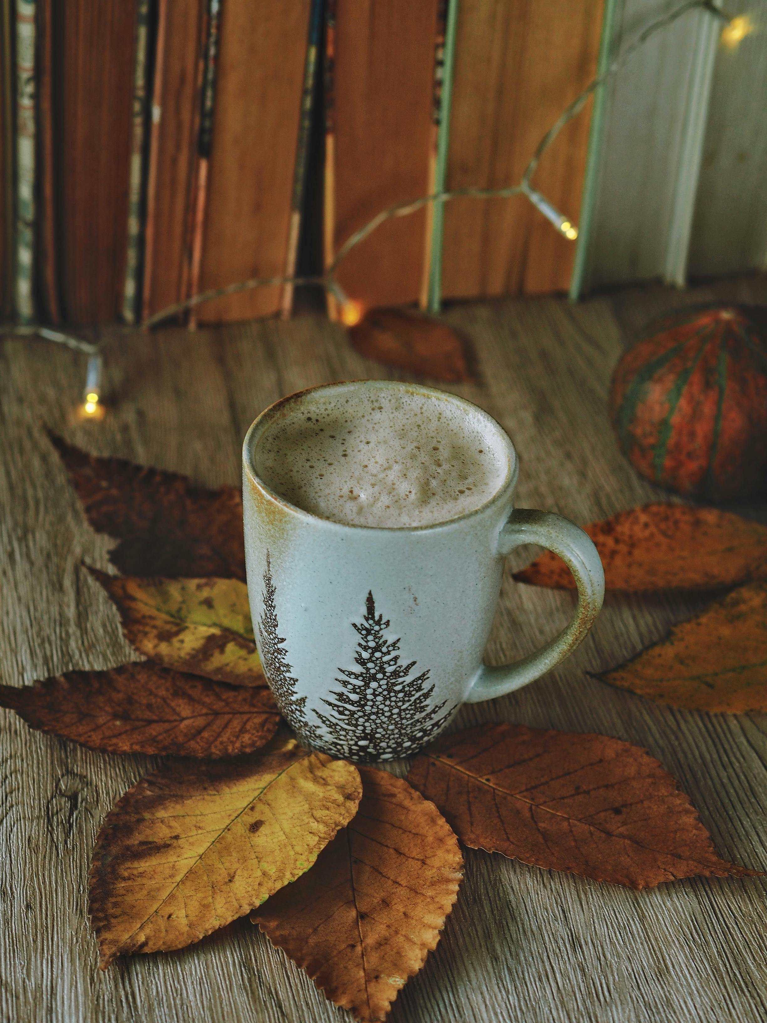 Warm autumnal setting featuring a coffee mug surrounded by dried leaves on a wooden table.