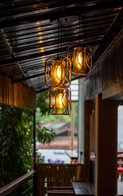 Three black-framed lantern pendants suspended evenly spaced from a white ceiling over a cozy outdoor seating area, blending matte metal with soft amber glow.
