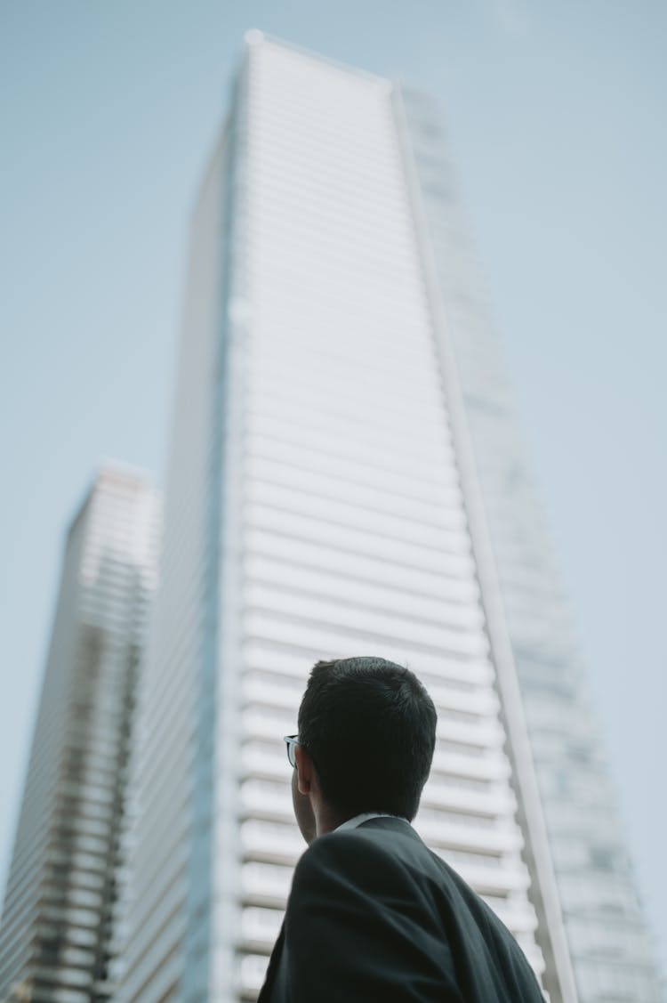 Back View Of Man Looking Up At A Skyscraper 