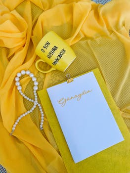 Vibrant yellow coffee mug on fabric with greeting note and pearl necklace for a cheerful morning setup.