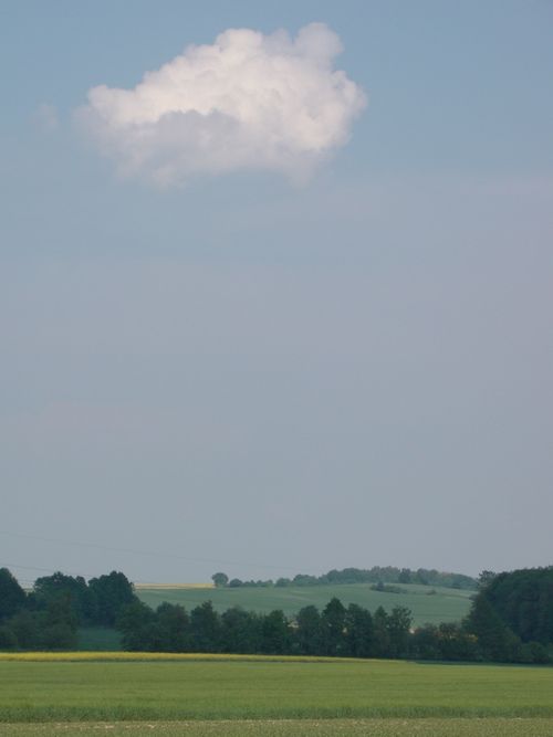 Free A peaceful landscape of a green field and solitary cloud against a blue sky, perfect for nature-themed projects. Stock Photo